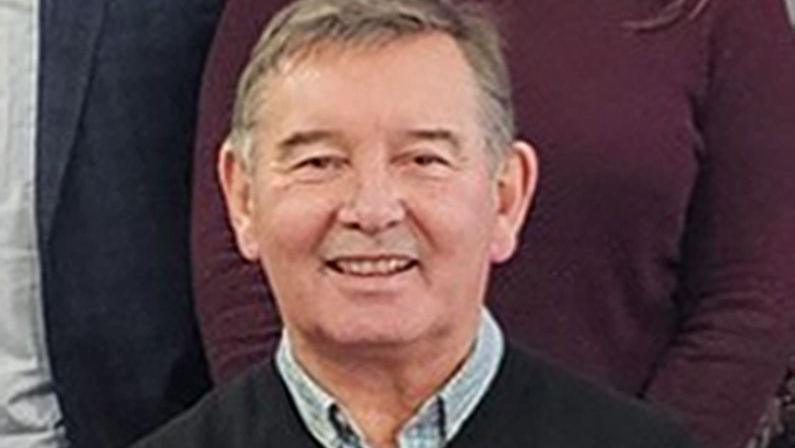 Peter Aitken wearing a blue collared shirt underneath a black jumper. He has grey hair and is smiling at the camera.