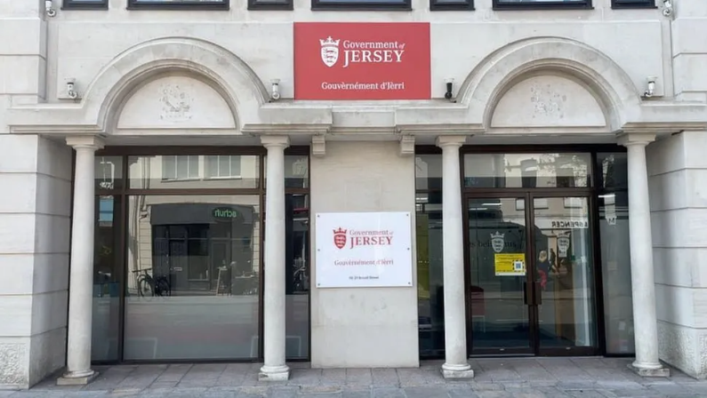 Front view of Government of Jersey building with name sign between two sets of twp columns with arched detailing on the front of the building and glass doors leading inside