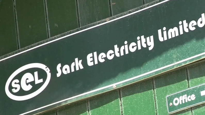 A green building with a slab with SEL - Sark Electricity Limited - logo on it. An office sign is visible bottom right.