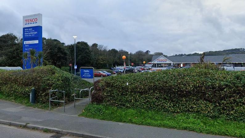 A street view image of a Tesco supermarket in Penzance. Hedges line the perimeter of the car park.