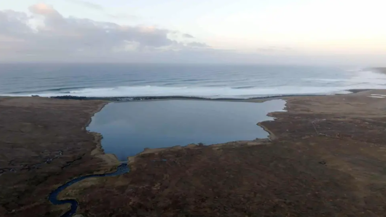 Sealladh bho gu h-àrd de mhòinteach ri taobh na mara. Tha loch anns an dealbh cuideachd.