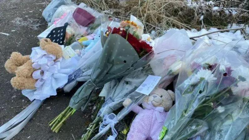 Bunches of flowers and two teddies lie on a woodland path.