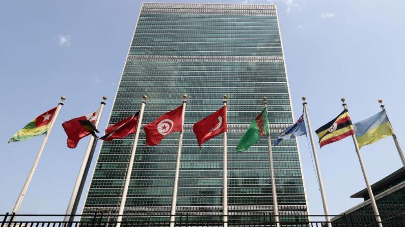 The UN building in New York seen from below, with various nations' flags flying at full mast.