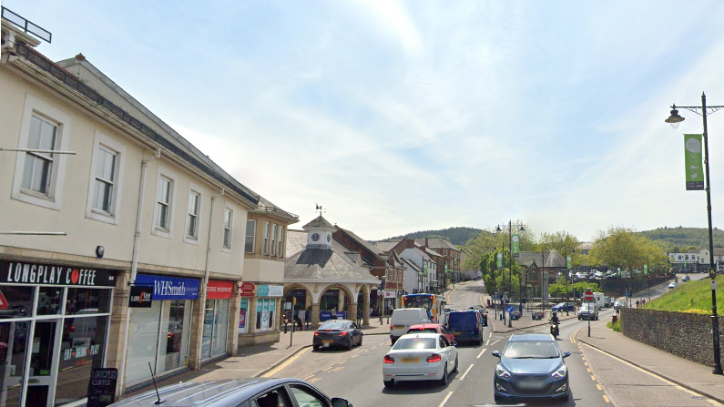 Google streetview image of Castle street in from of Castle court shopping centre, an outdoor mall with a gondola structure beside the road and then a row of shops. the street is busy with cars and you can see a coffee shop and book shop store fronts