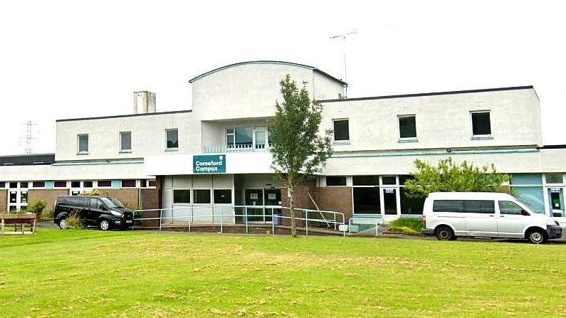 Google image of the main entrance at Corseford College in Jonstone. It is a two-storey building, painted white, with some pale green inserts along the windows and a grassy area in front of the entrance.