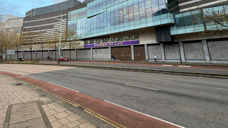 Concrete walled cinema with a two-floor glass window on the first and second floor. SHOWCASE is written in capitals on the wall, and a purple banner below it reads CINEMA DE LUX