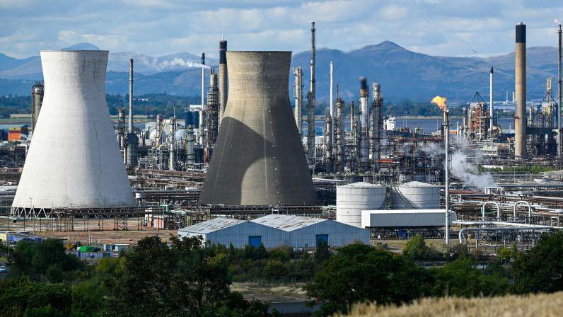 A general view of Grange mouth refinery with industrial towers, chimneys with trees mountains and water in the background.