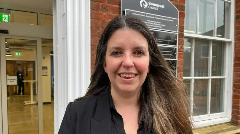 A head and shoulders photo of Councillor Federica Smith-Roberts. She has dark hair, is wearing a black shirt and jacket and is standing outside an office building.