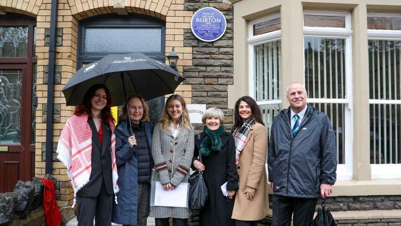 A group of people lined up outside a house, smiling at the camera