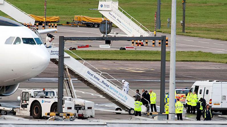 Abdelbaset Ali Mohmet al-Megrahi walks up the steps to board an aircraft at Glasgow airport on 20 August 2009. He is followed by three men in suits and police officers and other people in high vis clothing can be seen on the tarmac.