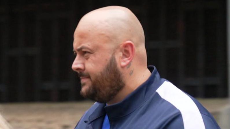 Dominique Saunders is led out of the court. He is wearing a blue tracksuit and is bald with a short dark beard.