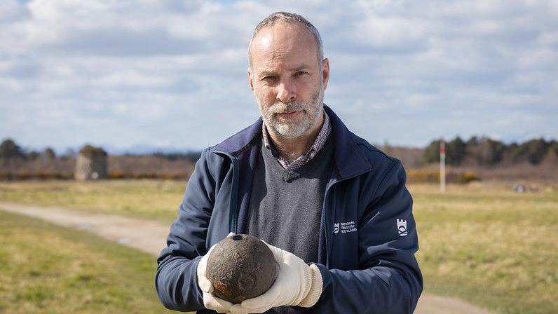 Ceannard arc-eòlais le Urras Nàiseanta na h-Alba Derek Sutherland leis an urchair moirteir 