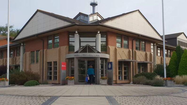 The exterior entrance of the Avon and Somerset Police Headquarters building in Portishead. It is a brick building with a concrete slab walkway and triangular white panelled roofs