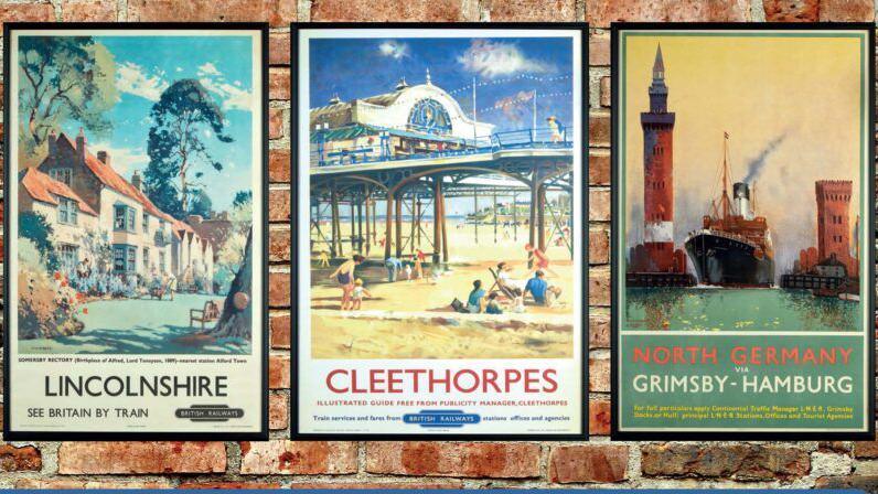 3 posters in a row - the one on the left depicts a village scene and says "Lincolnshire - see Britain by train". The poster in the middle is a picture of the pier at Cleethorpes in the sunshine with bathers on the beach.  The third poster depicts a large ship coming out of Grimsby harbour and says "North Germany via Grimsby - Hamburg".