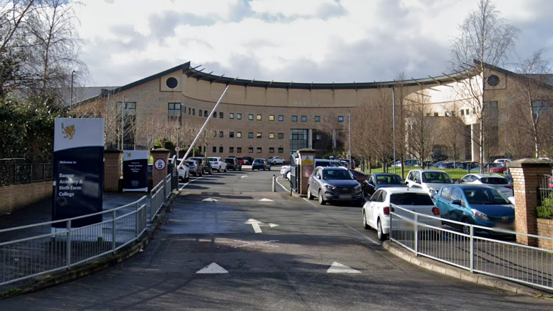 The front of Bangor Academy. There is a large brick building, slanted at each side. There is a car park in front of it.  