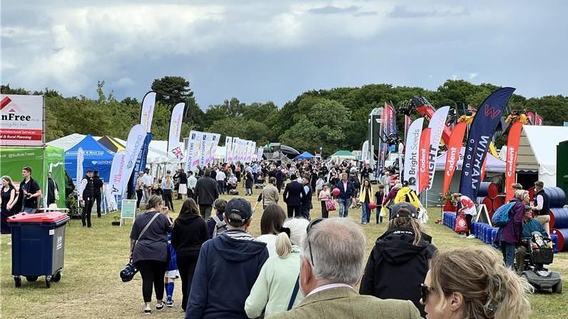 Visitors at the Suffolk Show walk through a large area that is lined with flags and stalls.
