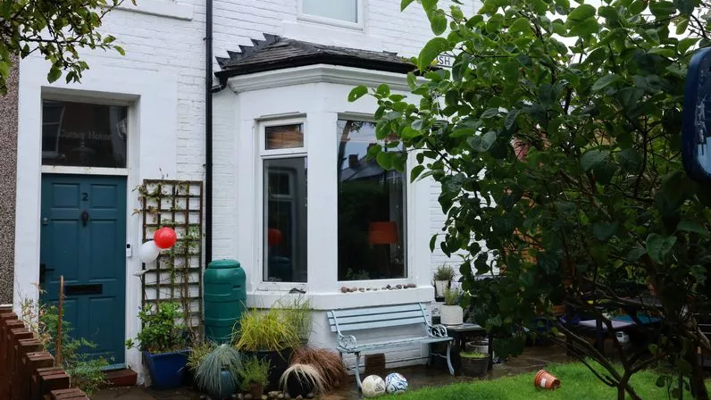 A house with a bay window, blue door and blue bench outside it.