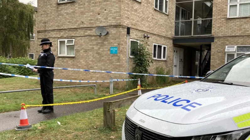 Police officer and police vehicle outside flats, surrounded by police tape