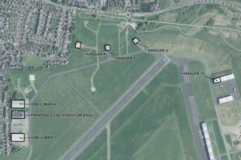 An aerial map of Solent Airport. The runway runs diagonally down the middle. Two Bellman hangers are on the left, while near the top four new hangars are proposed. A housing development borders the left and top of the image.