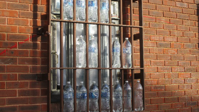 Fifteen plastic bottles outside a barred prison window, apparently ready to use for bottling hooch/illicit alcohol.