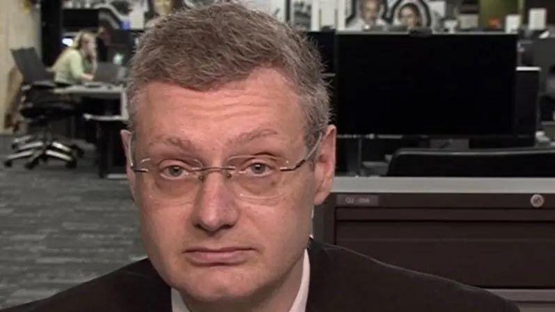 Joel Goodman sat at the BBC offices in Salford as he speaks to BBC Newsnight. He is wearing a suit and rimless glasses. 