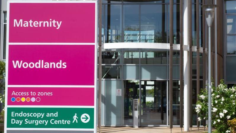 The glass-fronted two-storey entrance to Lister Hospital's maternity department, with a sign in bright fuschia and green listing the nearby departments.