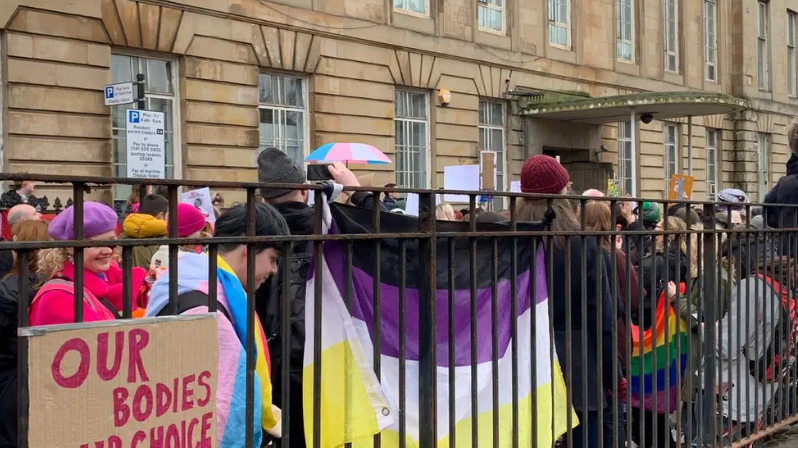 Pro-trans activists hold up flags and banners while protesting outside the Sandyford clinic in Glasgow in March