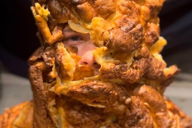 A boy covered in yorkshire puddings. Only his right eye and nose are visible underneath the crusty gooey goodness.