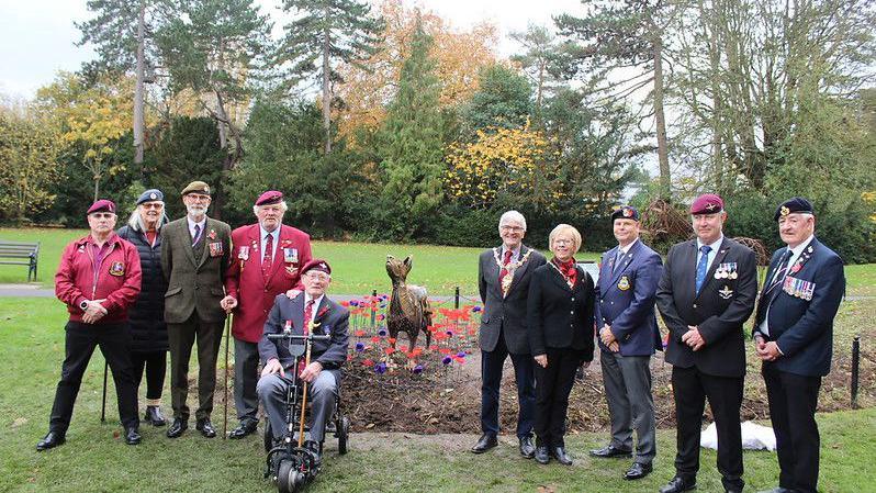 A group of ten people stand in front of the sculpture of Bing, some wearing army uniforms. 