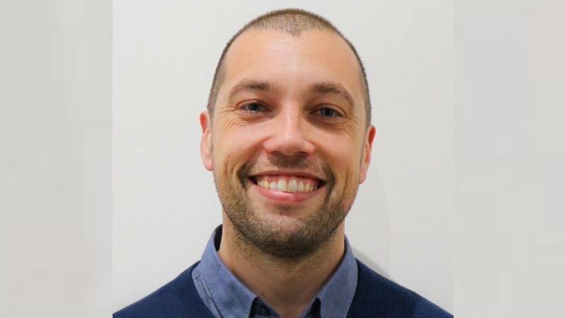 Head and shoulders shot of James Bromley. He has a buzz cut and is wearing a blue jumper.