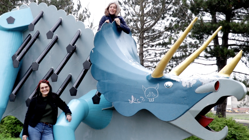 Susie Glatt standing in front of a blue Triceratops that Jude Keenan has climbed