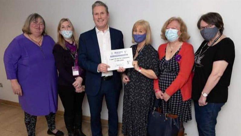 Sir Keir Starmer holding a white sign, as he stands alongside five women wearing Covid masks - they are all campaigning for compensation for Waspi women