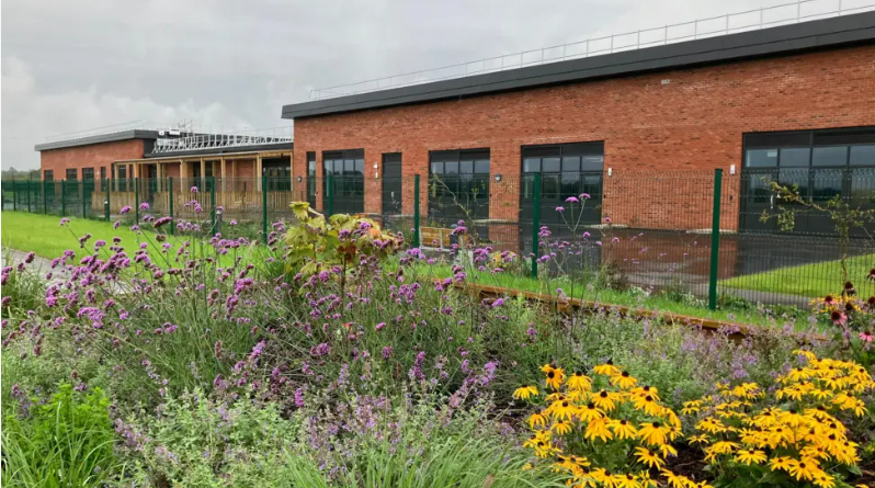 The outside of the school, with red brick buildings and flowers in the foreground.