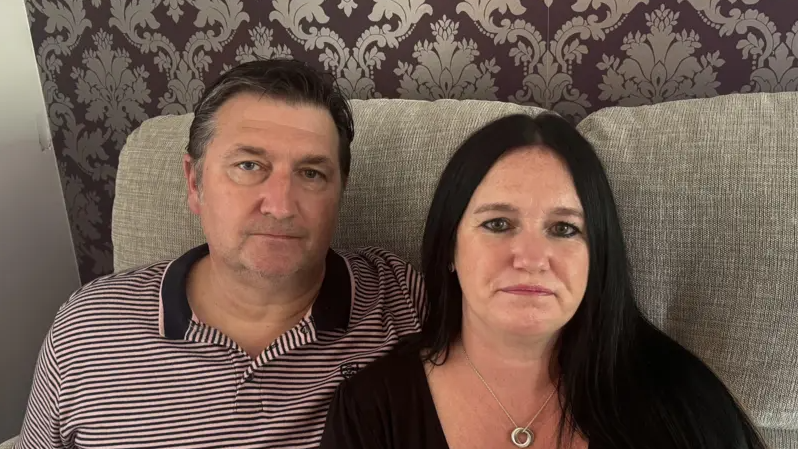 A man with dark hair and wearing a striped polo shirt with a woman with black hair wearing a black top