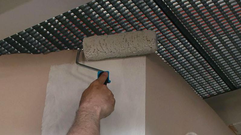 Stock image of a man using a paint roller with white paint on a wall