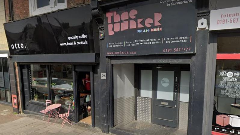 The Bunker music studio which has a black painted exterior with pink lettering for its name, with other shops on either side.