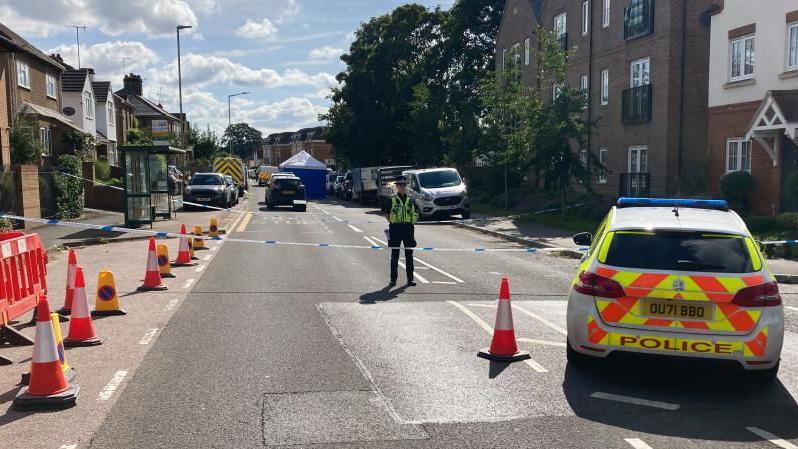 Railway Terrace, Kings Langley, closed off by police, with cones, police tape, police cars and a police officer standing in the road 