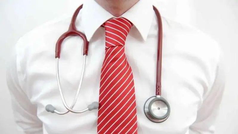 A close-up of a man wearing a white shirt and red and white striped tie, with a stethoscope around his neck.