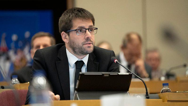 A head and shoulders picture of James Courtenay in a Southend City Council meeting, wearing a dark suit and tie, with a microphone and screen device in front of him