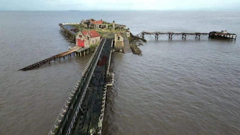 Shot of old crumbling pier, with planks hanging off taken from a drone above it 