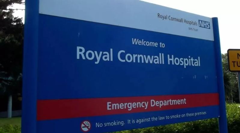 A blue, white and red sign that says 'Welcome to Royal Cornwall Hospital Emergency Department'. At the bottom of the sign another line says 'No smoking. It is against the law to smoke on these premises.'