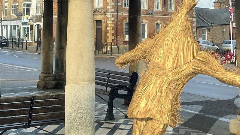 An augmented-reality Straw Bear at the Buttercross in Whittlesey. It is a cartoon looking straw bear that can only be seen through a smartphone