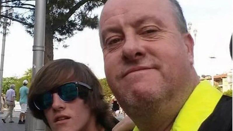 Mikey Rainsford, who has long brown hair and wears a pair of reflective sunglasses, poses for a picture with his father Michael Rainsford