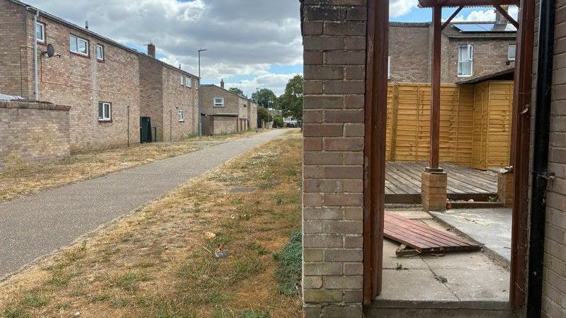 Garden gate of a house lying on the ground. It appears to have been kicked in. Other houses on the same estate can be seen in the background.