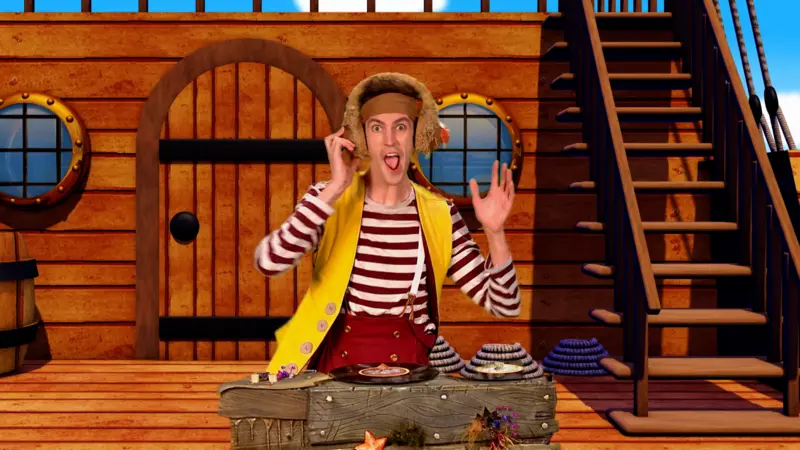 Seaweed character is standing behind some DJ decks with a ship background. He is wearing headphones.