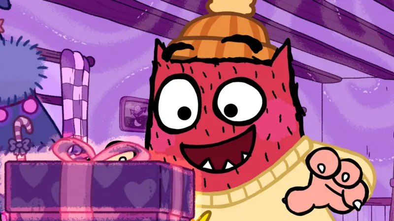 Love Monster is dressed in a yellow jumper and wooly hat and is looking excited staring at a present.