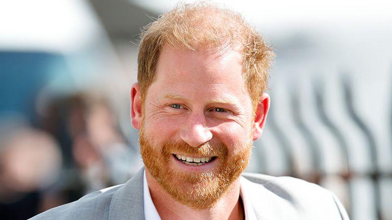 Prince Harry in light grey suit smiles at the camera