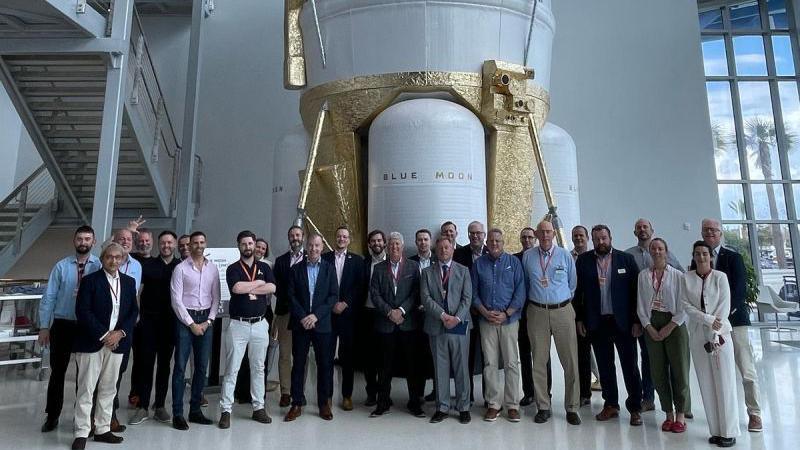 A delegation of space industry representatives standing in front of a Blue Moon lunar lander. The large craft is white with sections painted gold.