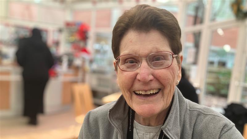 Betty Cobley looking into the camera. She is smiling, wearing glasses and a grey fleece jumper.