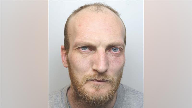 A police mugshot of John Whitfield, who has blue eyes, receding hair and a ginger beard